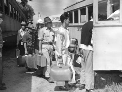 A group of Japanese men boarding a school bus at Amache Internment Camp. They carry suitcases.