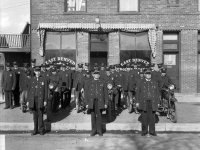 Black and white photo of a group of Denver police officers pose near a building with signage saying East Denver Police Station.
