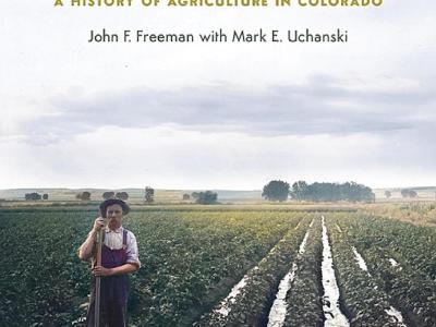 Photo of a book cover whose title is "Adapting to the Land: A History of Agriculture in Colorado." Below the title are the author' names: John F. Freeman with Mark E. Uchanski. The photo on the cover is across the cover's entirety from edge to edge, and is what appears to be an old photo, recolored, of a farmer stanging amongst rows of crops that stretch off far into the distance. Short leafy plants cover the linear mounds of early, and water flows between the mounds. The farmer is standing with a shovel.