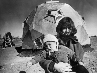 A woman holds a child in front of a geodome in a black and white photo