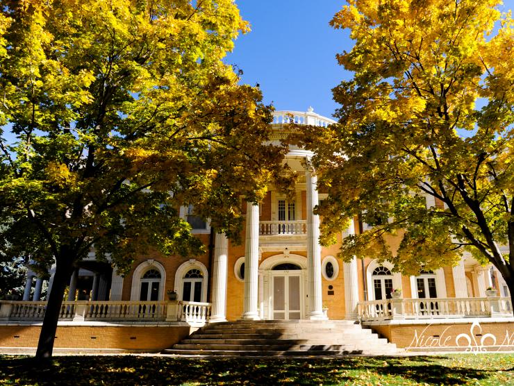 A photograph of the front facade of the Grant-Humphreys mansion during the day, showing the columned front stairs flanked by trees.