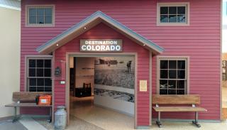 Opening to Destination Colorado exhibit, showing the facade of a red house with entrance to the exhibit.