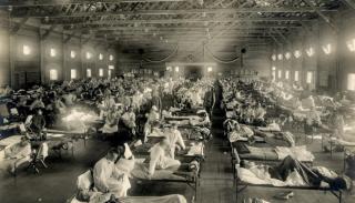 Black and white photo of rows of beds in a large room. The beds are all full with people suffering from influenza during the 1918 Flu Pandemic.