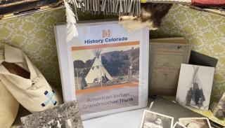An artifact kit holding a collection of artifacts such as a hide and native american shoe as well as photos on a table. 