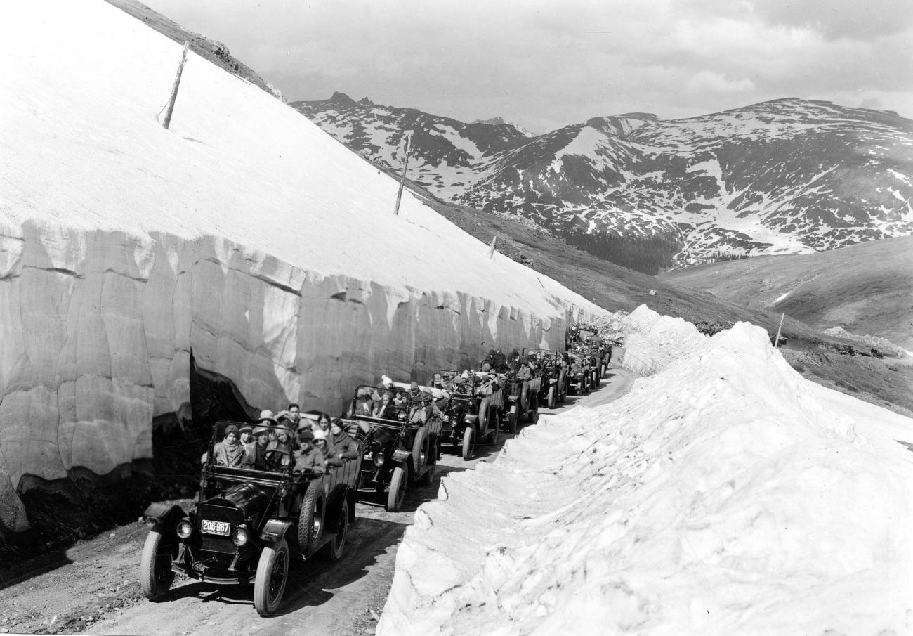 A line of automobiles, flanked on each side by many feet of snow, on Fall River Road in Rocky Mountain National Park