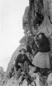 A group of men and woman pose beside a steep cliff near the summit of Longs Peak.