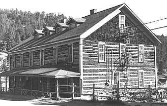 A pioneer log style building with hewn log, side gable with shingle gables.