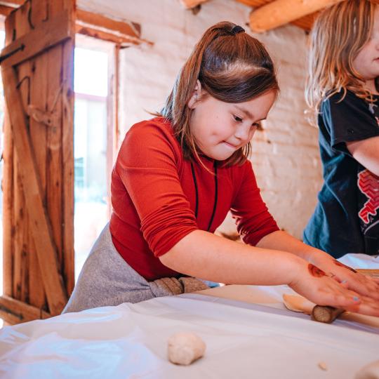 Two kids make tortillas by rolling out dough