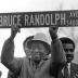 Bruce Randolph holding up a street sign which reads: "Bruce Randolph, Ave."